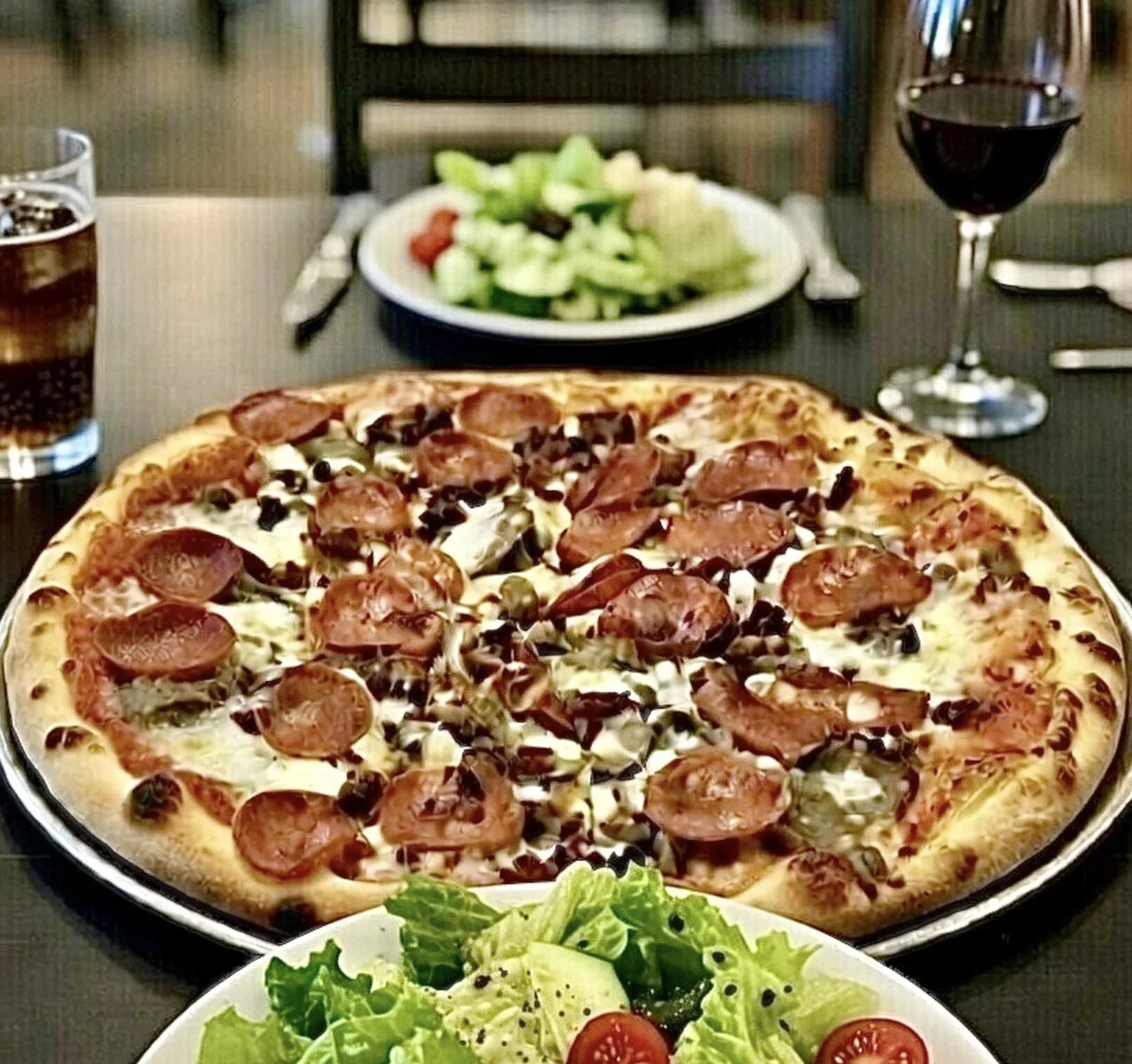 A specialty pizza served at the table with salad and wine