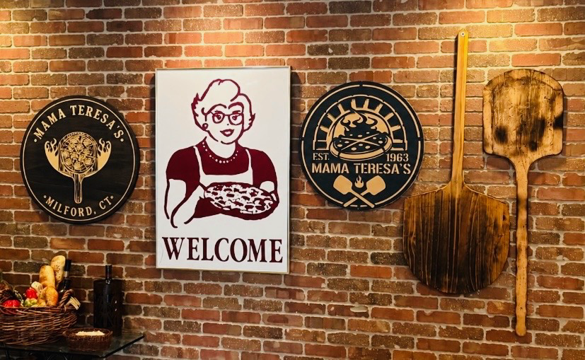 The welcome wall at Mama Teresa's in Milford, with vintage-style pizza and Mama Teresa's signage